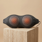ArchZen heated lumbar massage cushion, slim dark-gray peanut shape with two dimpled massage zones, on a travertine pedestal