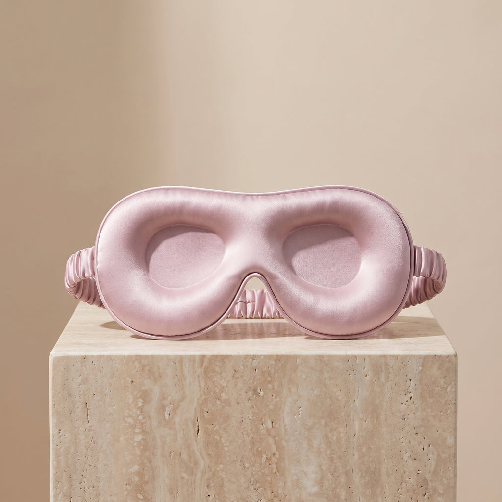 DreamZen pink contoured silk sleep mask on a travertine pedestal