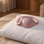 Pink silk sleep mask resting on a white linen bedroom pillow