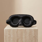 Black DreamZen contoured silk sleep mask on warm stone