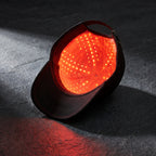FollicZen black cap with red LED glow on dark charcoal stone surface