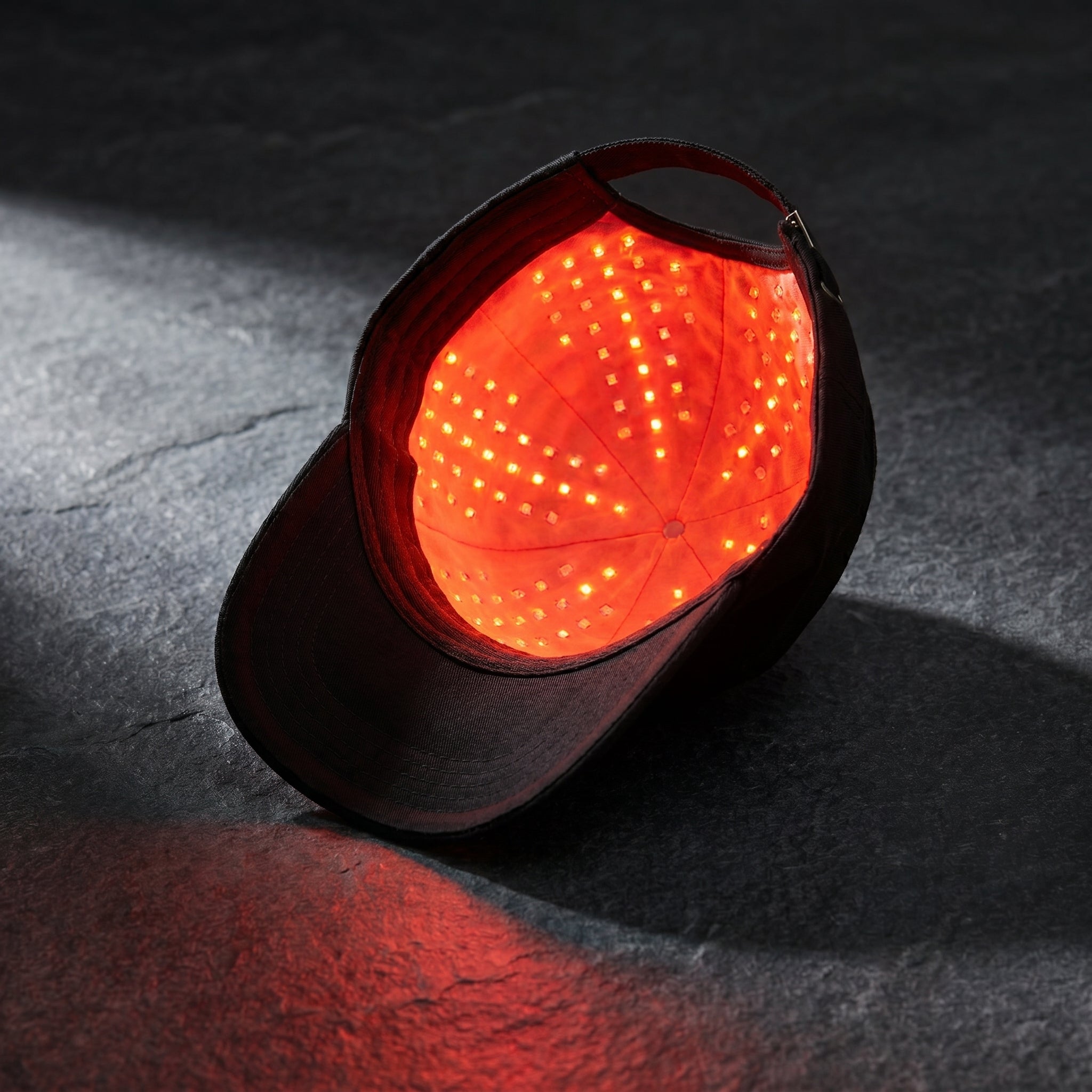 FollicZen black cap with red LED glow on dark charcoal stone surface