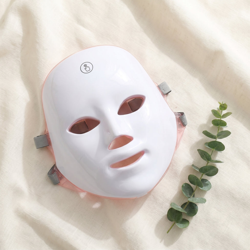 GlowZen LED face mask lying on cream linen with a eucalyptus sprig