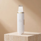 PoreZen scrubber in white with gold accents on a stone pedestal