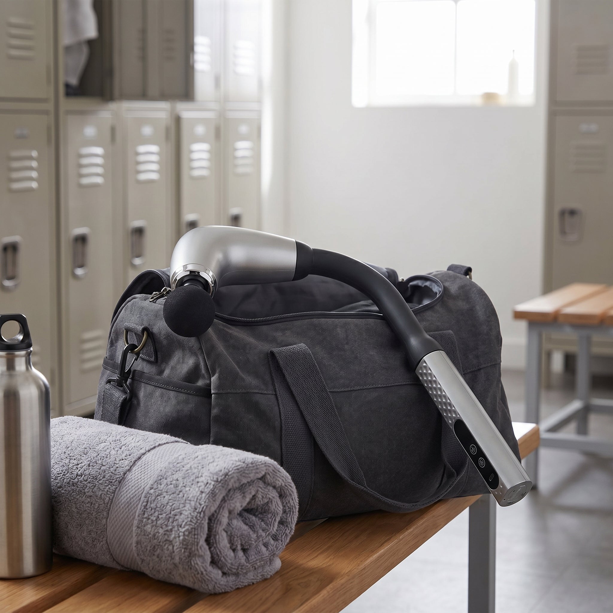 Silver massage gun resting on a gym duffel bag with towel