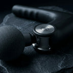 PulseZen Pro percussion massage gun on dark charcoal surface with dramatic side lighting