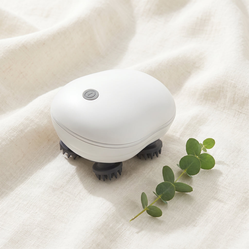 ScalpZen head massager resting on cream linen beside a eucalyptus sprig