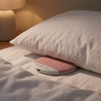 SnoozeZen pink speaker tucked under a white pillow on linen bedding