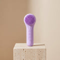 SonicZen purple silicone facial cleansing brush on a travertine stone pedestal