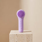 SonicZen purple silicone facial cleansing brush on a travertine stone pedestal