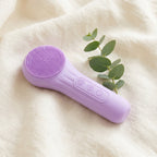 Purple SonicZen brush resting on cream linen beside a eucalyptus sprig