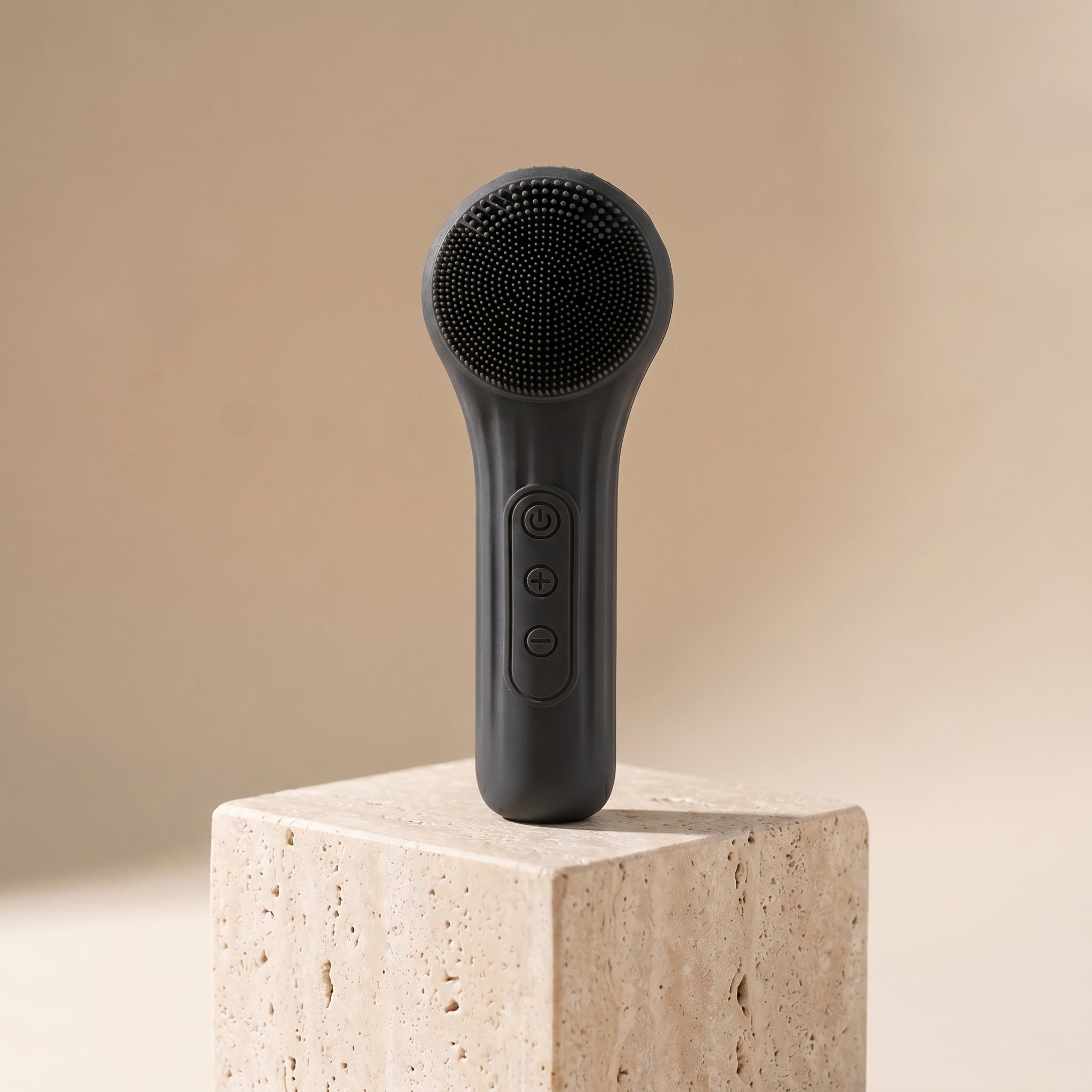 SonicZen brush in charcoal black on a travertine pedestal in warm light
