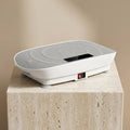VibeZen compact vibration plate on travertine pedestal warm studio light
